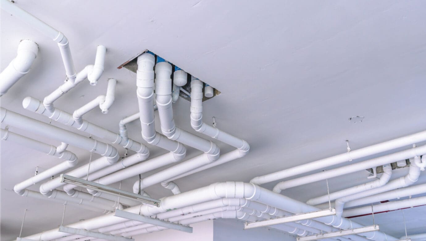 Plumbing contractors installing overhead water and sanitary mains on a commercial construction project in Ohio