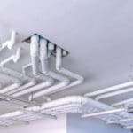 Plumbing contractors installing overhead water and sanitary mains on a commercial construction project in Ohio