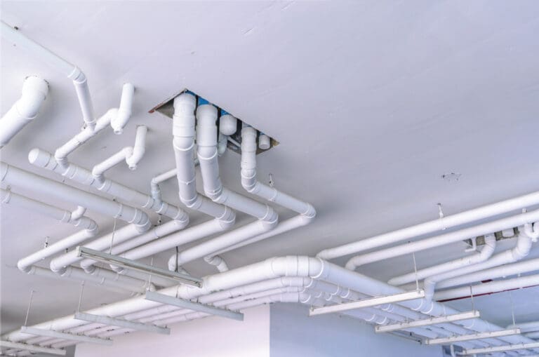 Plumbing contractors installing overhead water and sanitary mains on a commercial construction project in Ohio