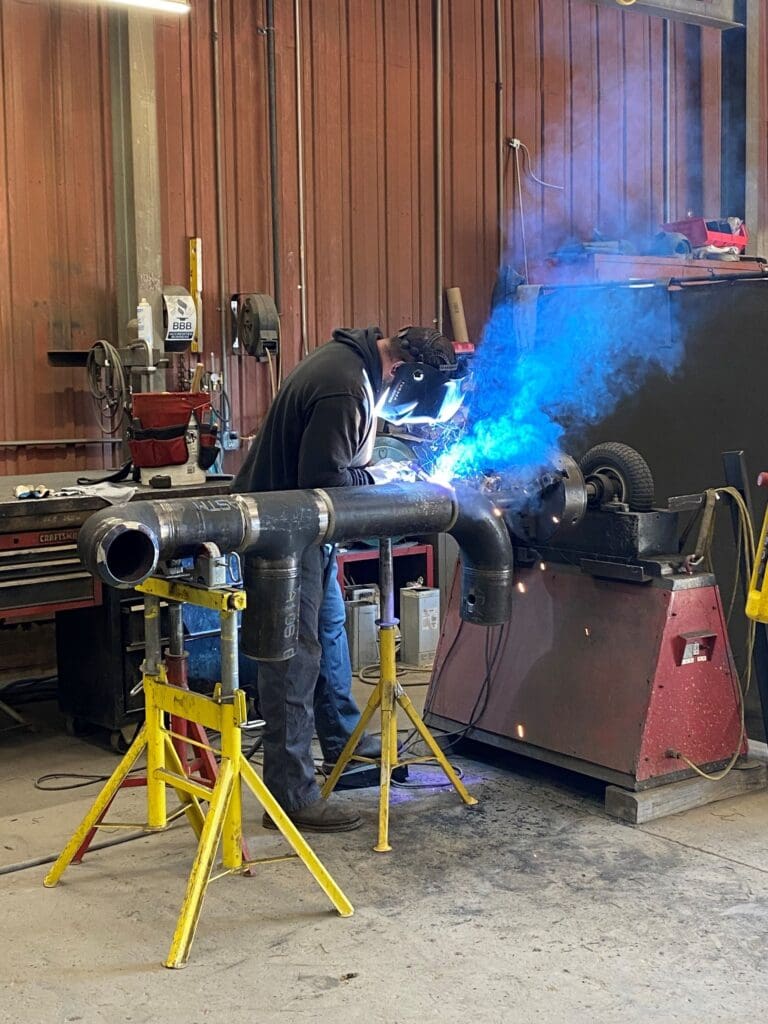 Wilkes welder joining pipe sections on roller stands in the fabrication shop