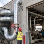 Cartridge dust collection system outside a plant wall, galvanized ductwork, and a technician adjusting a blast gate
